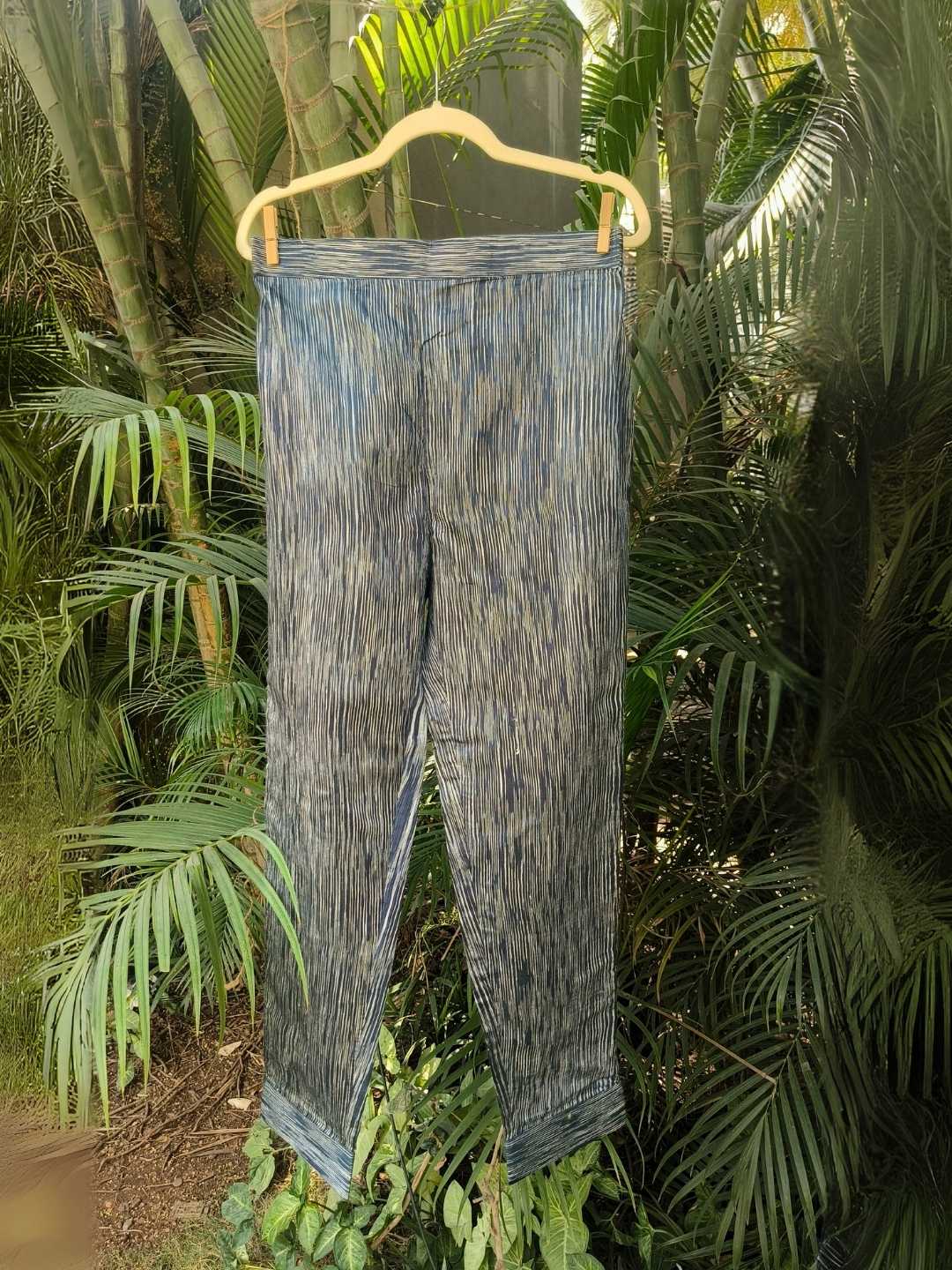 Siona Pants- Handwoven Tussar Silk | Jhultaru by Jhultaru. Fabric: 100% Handwoven Tussar Silk  Color: Indigo with natural striationsStraight, tailored fit. Ankle lengthElasticated back waistband for comfortClean hem finish for a refined look- Handwoven tussar silk Siona Pants in striated indigo tones. Straight fit, ankle length, and artisanally crafted comfort. A wardrobe staple that is eco-friendly and sustainable